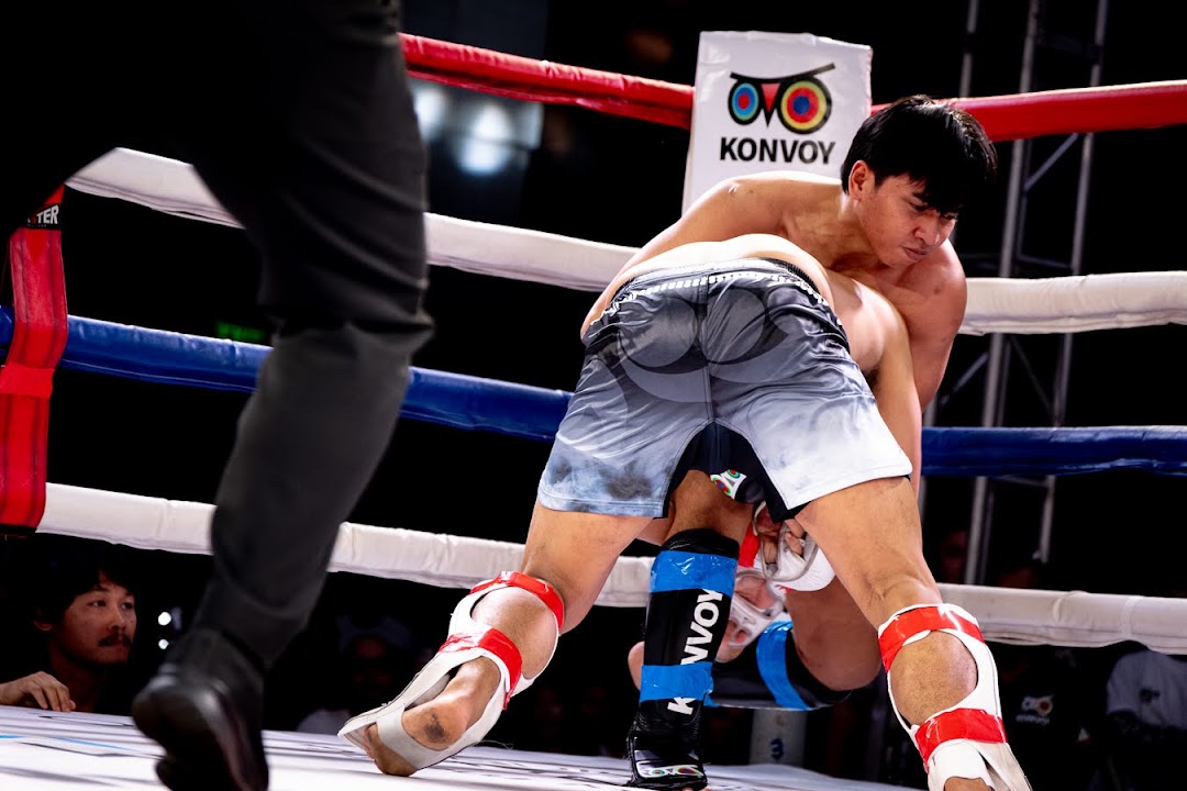 An MMA fighter drives into a takedown attempt near the ring ropes.