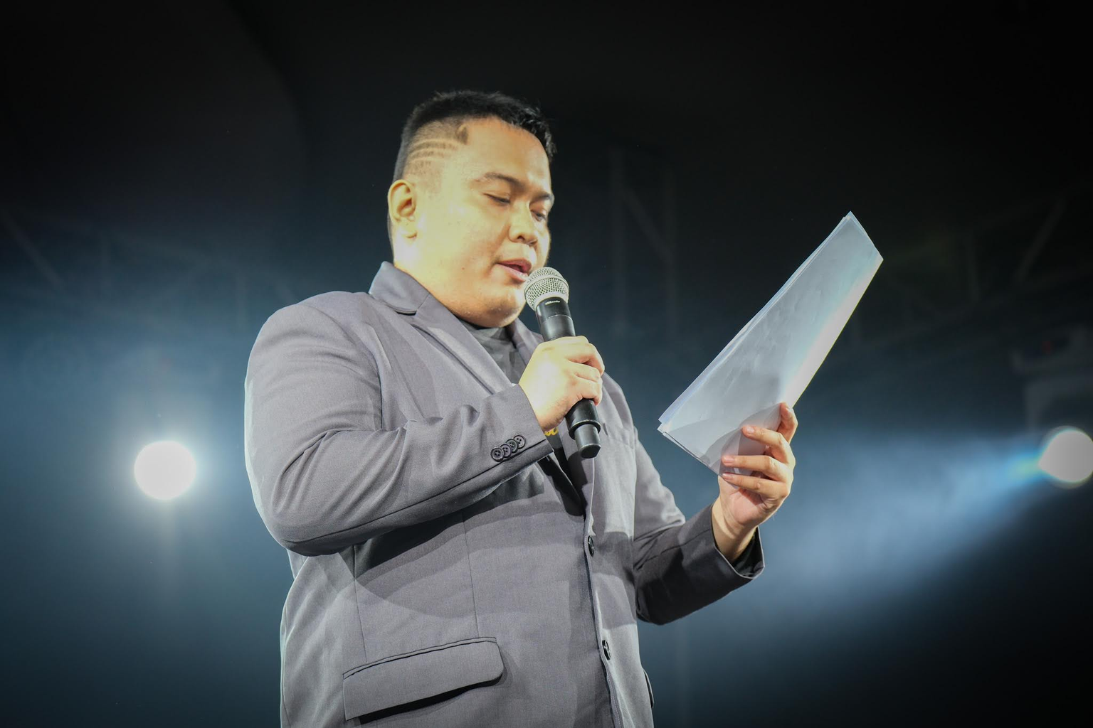 An announcer reads from a sheet of paper while speaking into a microphone at Konvoy 03.