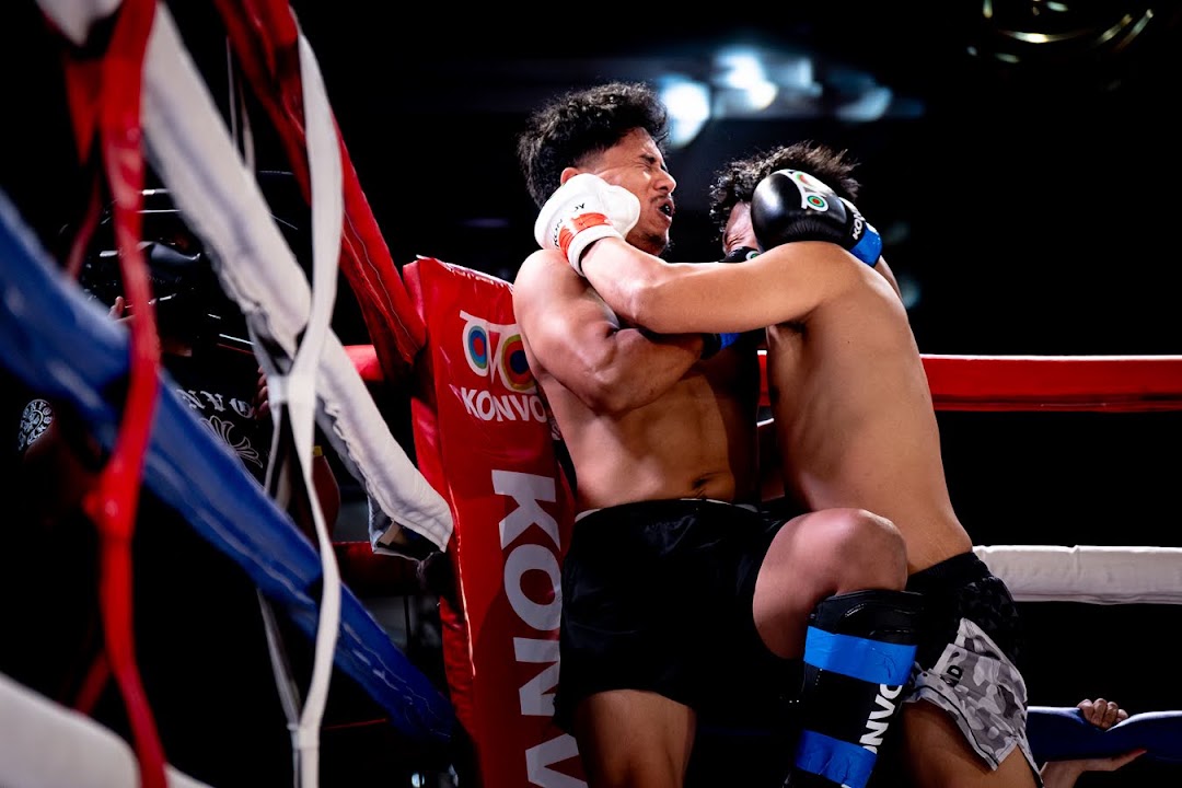 Two MMA fighters battle for control in the clinch against the ring ropes.