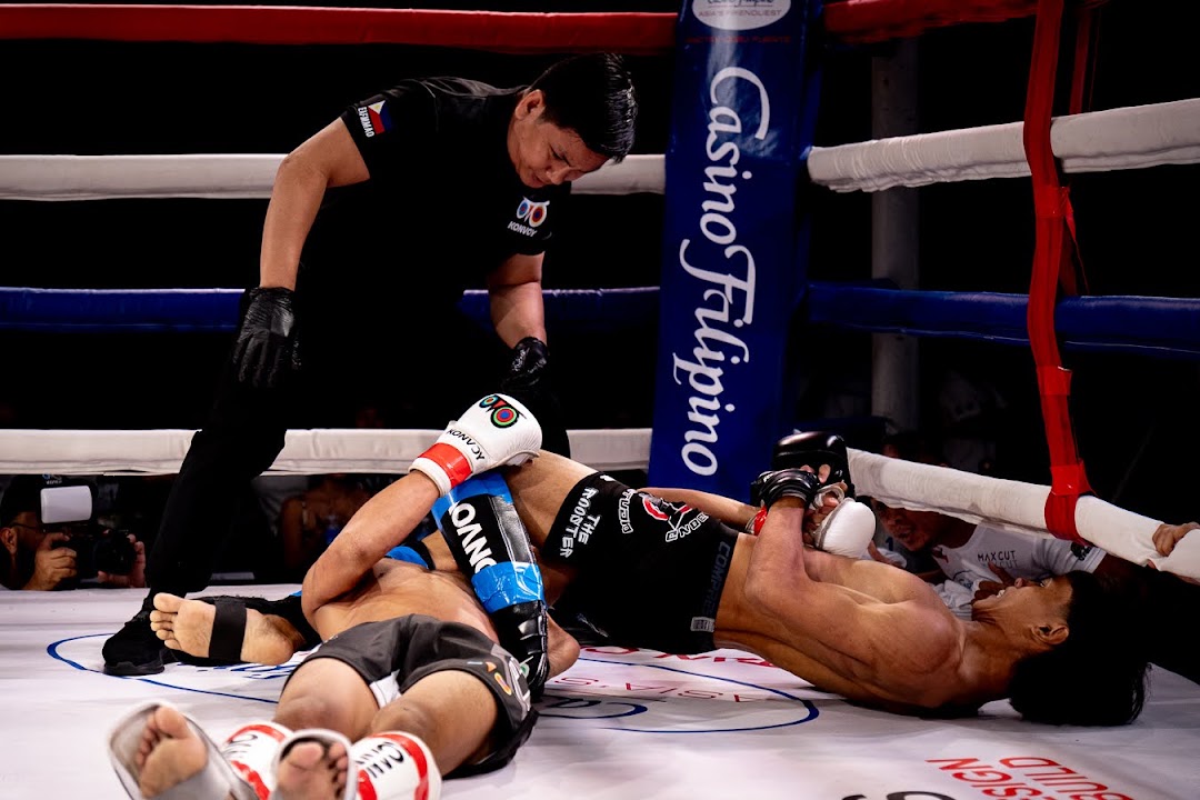 Two MMA fighters struggle for submission control on the mat as the referee watches.